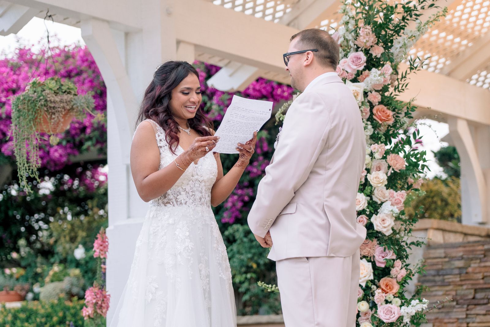 Bride laughing as she reads her vows under a floral gazebo