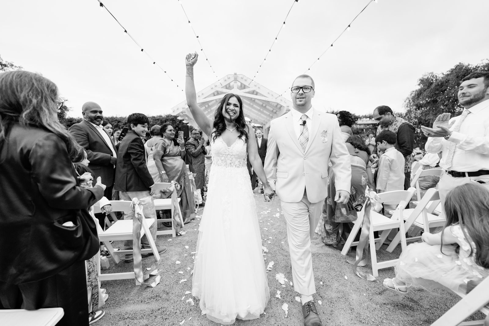 Bride raising her fist in celebration as the newlyweds walk back up the aisle, in black and white