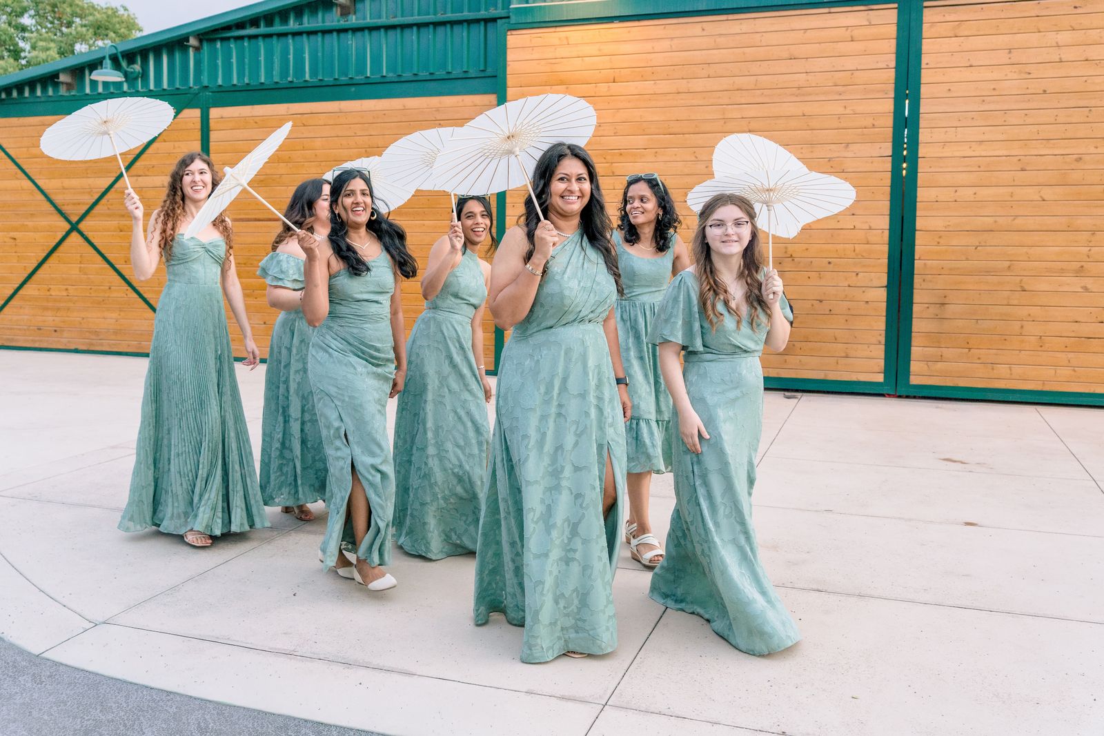Bridesmaids in sage dresses walking with white paper parasols